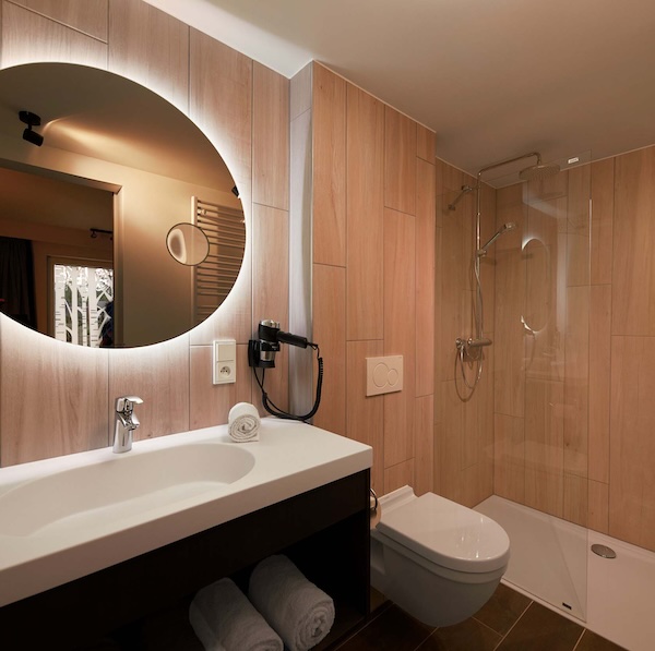 Salle de bains d'hôtel avec carrelage mural en faux bois et WC suspendu entre la douche et le plan vasque